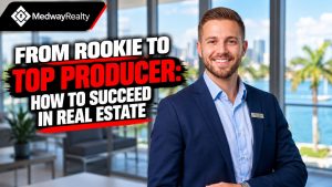 Real estate agent in a navy suit smiling in a high-rise office with a waterfront view, illustrating Medway Realty's guide on going from rookie to top producer